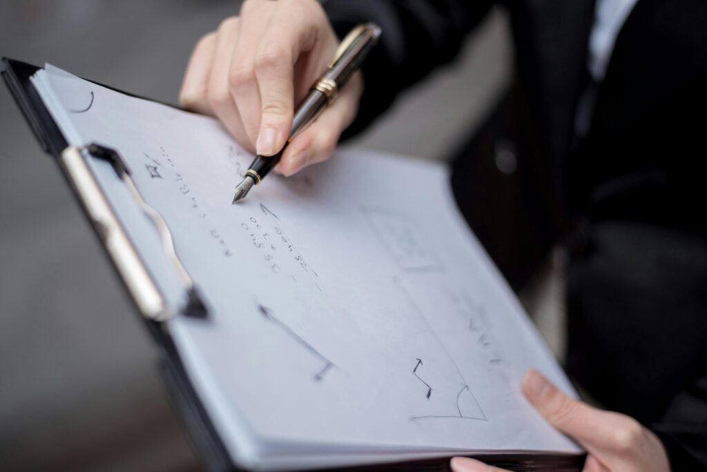 Home A person writing on a clipboard using a pen, focusing on the hand and paper.